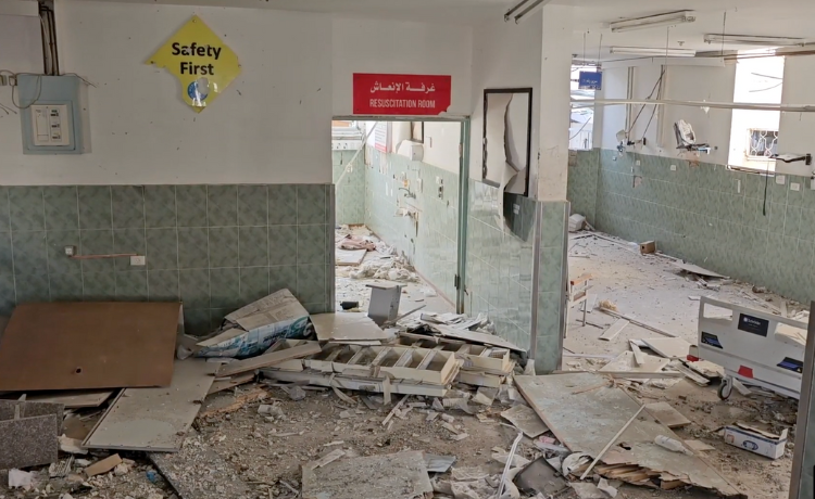 The interior of a health facility covered in debris, with a red ‘Resuscitation Room’ sign still hanging above a doorway