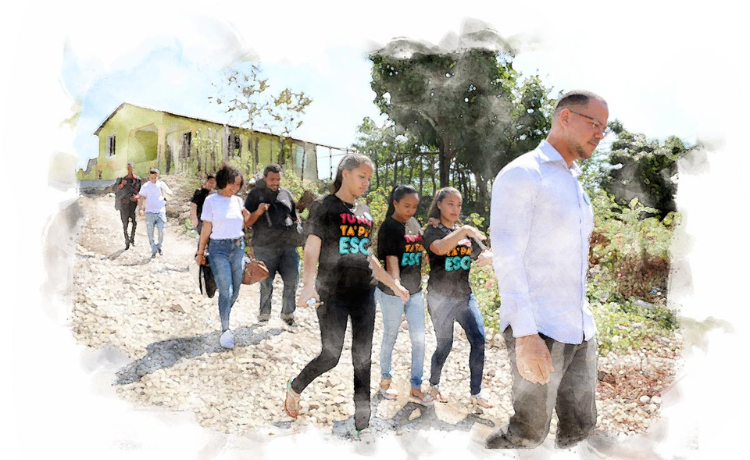  A slightly blurred image of a man in a white shirt walking down a hill in ront of a yellow house, followed by a dozen young people